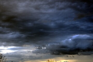 Dramatic dark storm clouds gather in the sky, creating a moody atmosphere with hints of light peeking through, showcasing nature's powerful weather phenomena