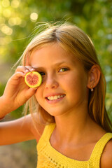 Blonde girl holding fig halves to her eyes on a sunny day, laughing and playing playfully,...