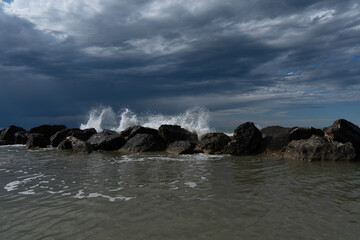 Waves crash on rocks under a dramatic sky. The water flows gently in the foreground, contrasting...