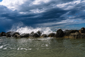 Waves crashing against rocks under a dramatic sky. Seascape scene with rough waters and dark clouds.
