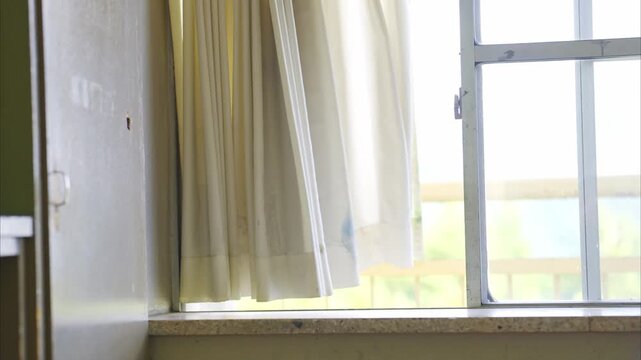 学校の教室の窓際で風に揺れる白いカーテン