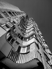 Monochrome low-angle view of a tall, modern building with a distinctive, rippling facade and rows of windows, against a dark sky