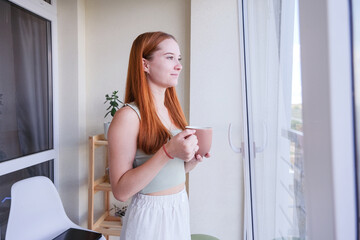 Woman drinking tea from the mug standing in the balcony