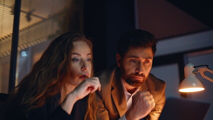 Naklejka premium Worried coworkers working late staring computer screen in dark office closeup