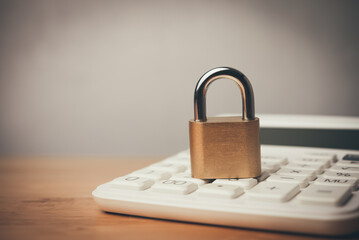 Padlock and white calculator on wooden table with white wall background copy space. Save money,...