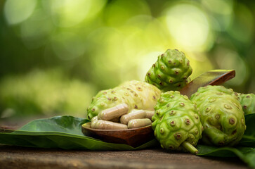 Noni fruits and powder packed in capsules on natural background.