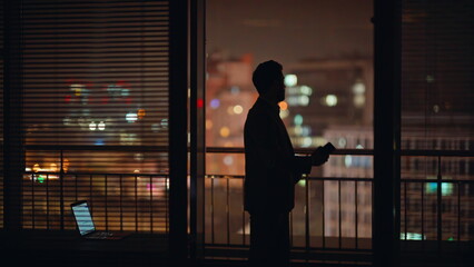Late night businessman messaging smartphone near panoramic window. Man resting