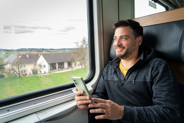 Hombre sonriente usando su celular mientras viaja en tren, sentado en la ventanilla