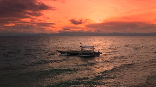 Traditional Filipino outrigger boats floating on the ocean during a vibrant orange and red sunset with distant islands, Boracay, Philippines.