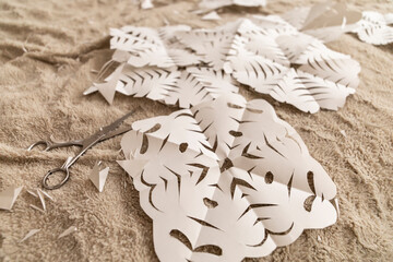 A detailed craft session showcases paper cutouts in a floral design, scattered on a soft surface. Scissors are nearby, illustrating the artistic process of creation