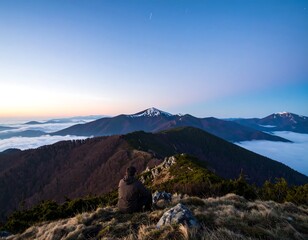 A serene mountain vista at dawn.  A person sits contemplatively on a peak