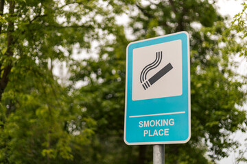 A blue and white sign displays a smoking symbol, indicating a designated smoking area located in a...