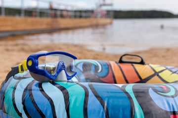 Brightly colored inflatable ring rests on the sandy shore of a lake, paired with snorkeling...