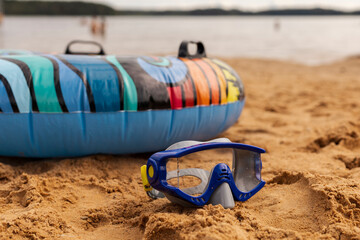 Bright inner tube sits on the warm sand next to a snorkel mask, with calm waters in the background....