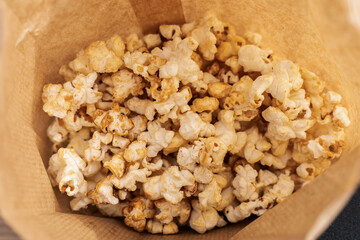 Freshly popped popcorn fills a warm brown paper bag, inviting enjoyment during a cozy movie night at home or a casual snack break with family and friends