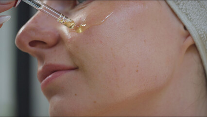 Young woman applies skincare serum by patting and gently massaging the face, close up shot....