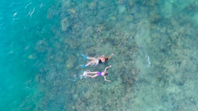 Aerial view of a woman and a young girl snorkeling with fins and masks in clear, shallow ocean water over a coral reef, Boracay, Philippines.