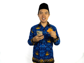 A happy Indonesian civil servant stands holding an orange card and a cell phone.