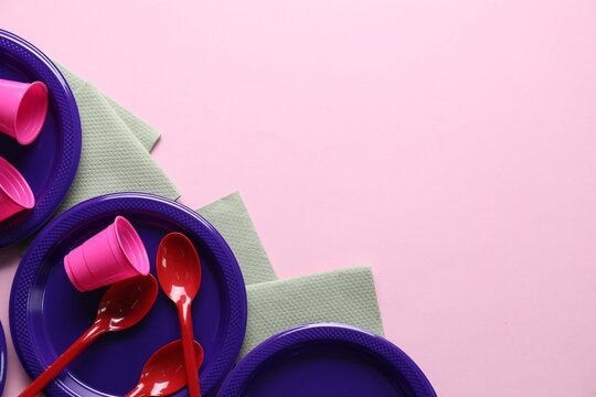 Set of disposable plastic tableware and paper napkins on pink background, flat lay. Space for text