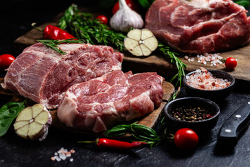 Raw pork cuts on a wooden board with herbs and tomatoes, ready to be cooked