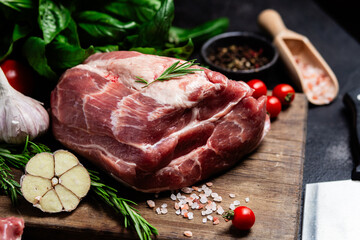 Raw pork cuts on a wooden board with herbs and tomatoes, ready to be cooked