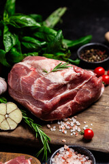 Raw pork cuts on a wooden board with herbs and tomatoes, ready to be cooked