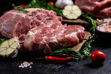 Raw pork cuts on a wooden board with herbs and tomatoes, ready to be cooked
