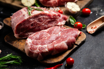 Raw pork cuts on a wooden board with herbs and tomatoes, ready to be cooked