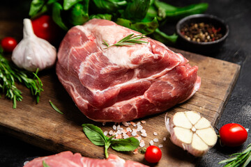 Raw pork cuts on a wooden board with herbs and tomatoes, ready to be cooked