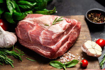 Raw pork cuts on a wooden board with herbs and tomatoes, ready to be cooked