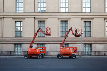 A symmetrical photograph of two bright orange articulated boom lifts parked on an empty city street...