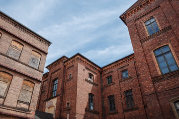 A low-angle photograph of a massive, historic industrial building made from dark red brick, set against a blue sky with clouds.