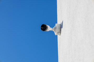 Security camera positioned on a white surface captures the bright blue sky, ensuring surveillance...