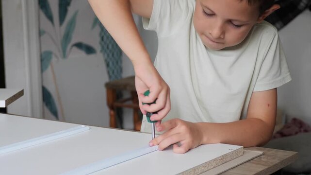 Boy assembling DIY furniture - A focused young boy carefully uses a craft knife to mark a line while assembling white flat-pack furniture