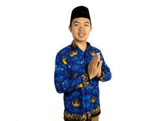 An Indonesian male civil servant wearing a blue Batik Korpri uniform poses with a respectful greeting gesture, standing in front of a white background. Civil servant concept PNS.