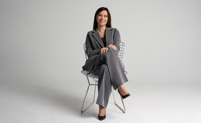 Portrait of a cheerful young businesswoman sitting in a chair against white background.
