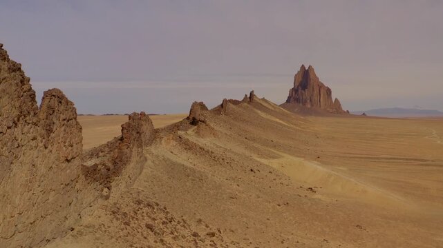 Spectacular 4K aerial footage of Shiprock (Ts&eacute; Bitʼaʼ&iacute;), the iconic volcanic rock formation towering above the high desert of northwestern New Mexico. Rugged badlands, dramatic desert terrain, and exp