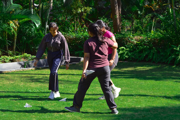 In a green tropical park, three teenage girls bend and move around happily to collect their paper...