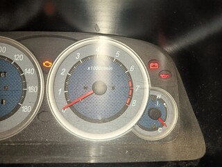 Close-up view of a dusty car's instrument cluster showing a tachometer, fuel gauge, and illuminated warning lights.