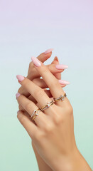 Elegant woman's hands with stylish rings and manicured nails against a pastel gradient background.