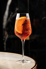 Refreshing cocktail with orange slice and ice cubes in a tall wine glass, served on a marble table....