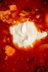 Traditional Russian-Ukrainian soup solyanka served with sour cream and fresh herbs. Rich, hearty broth with smoked meat, pickles, olives, lemon slice, and flavorful spices. Close-up of hot homemade di