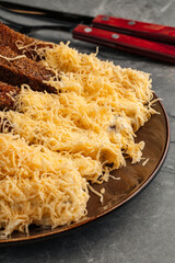 Crispy rye bread toasts with melted cheese served on a plate. Traditional garlic croutons made from dark bread topped with grated cheese. Close-up of rustic snack, popular appetizer for beer and casua