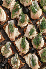 Obraz premium Traditional sandwiches with black rye bread and salted herring, served with onion and herbs. Classic Eastern European appetizer on a rustic wooden table
