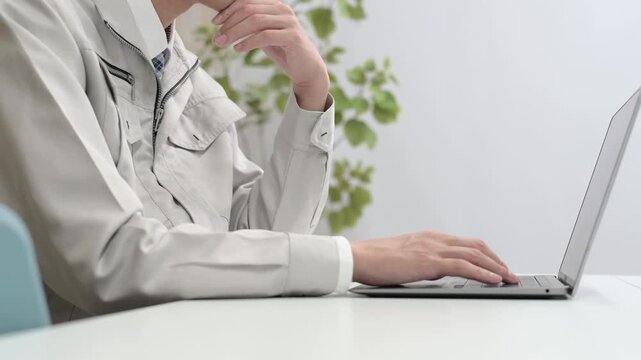 作業服を着てパソコン作業をする男性の手元