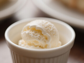 Close-up of a creamy vanilla ice cream scoop served in a white ceramic cup. Soft focus background with warm lighting creates a cozy dessert presentation.
