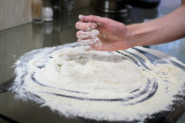 Hand Sprinkling Flour on Dough on Glass Table During Baking Preparation Process