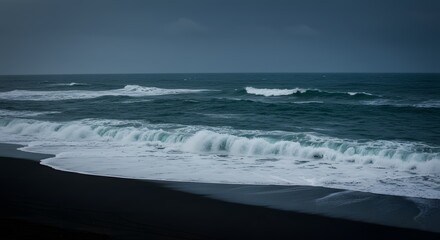 Fototapeta premium Serene coastal view of crashing waves on a dark sandy beach under a moody sky at dusk