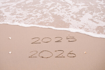 Handwritten inscription 2025 and 2026 on the beach in the sunset time. The concept of Goodbye 2025 and Happy New Year 2026