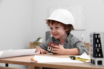 Choice of profession. Little kid in hard hat exploring house model at table indoors